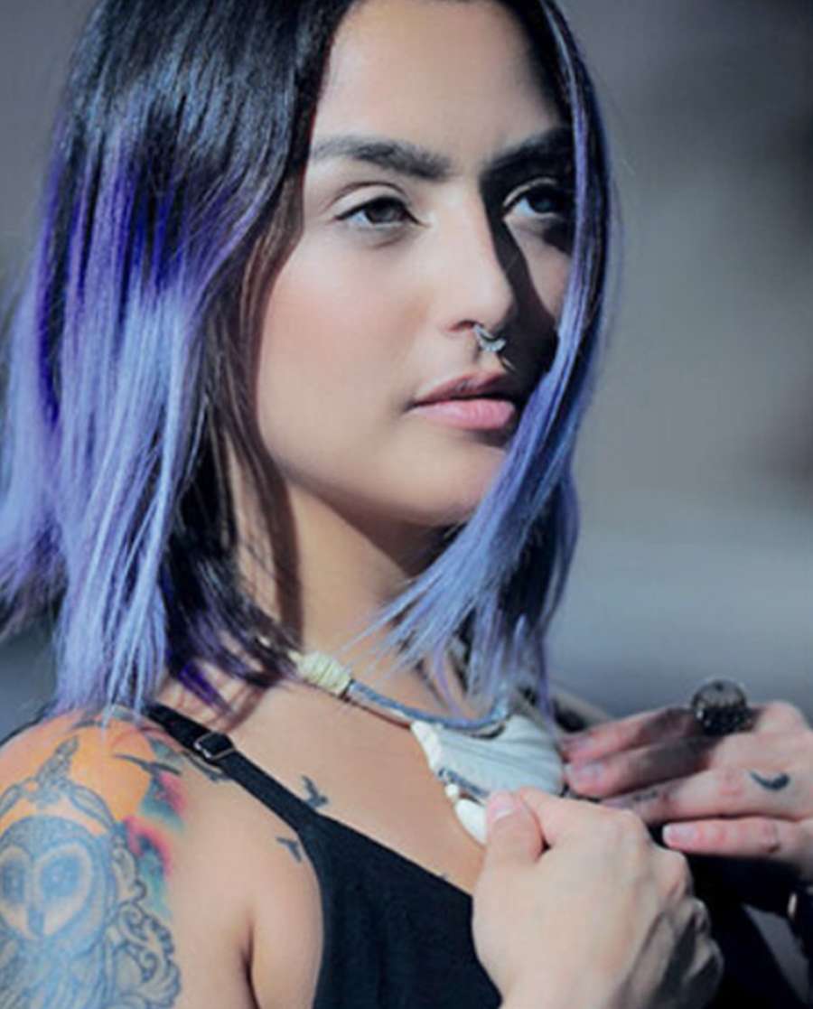 Portrait of a woman with blue and violet hair, a nose ring and a tattooed shoulder, fastening a necklace
