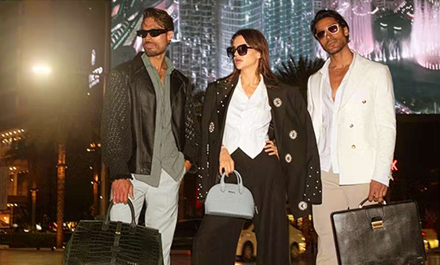 Two men and a woman in sunglasses standing on a city street at night, each holding a leather bag