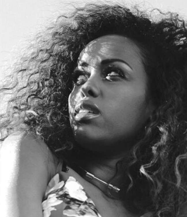 Black and white portrait of a woman with full curly hair, looking up over her shoulder