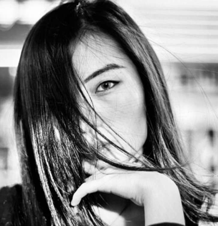 Black and white portrait of a woman with long dark hair blowing across her face, one eye visible