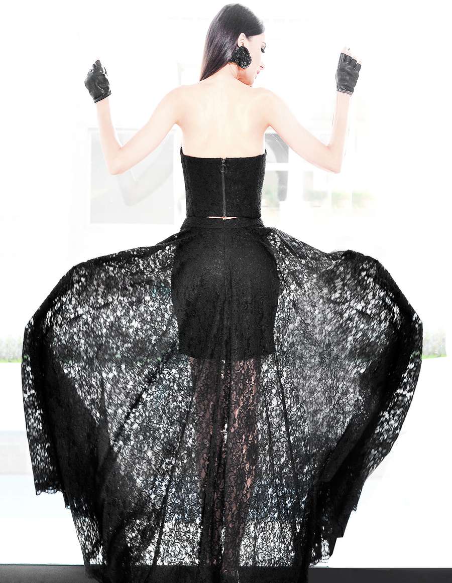 A woman seen from behind in a black lace gown, arms raised