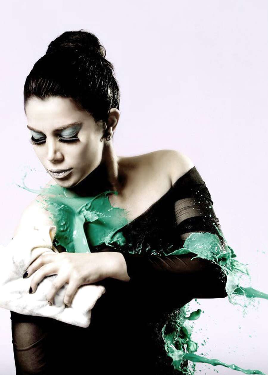 A woman in a sheer black top, splashed with green paint